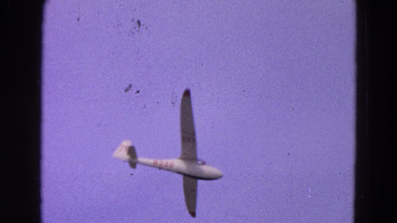White glider banking in a purple-blue sky with dark film borders.