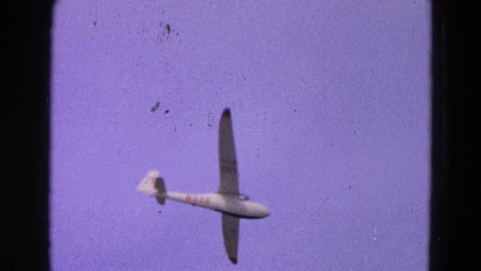 1964 8mm frame of a white glider with red markings banking against a purple-blue sky near Washington, DC.