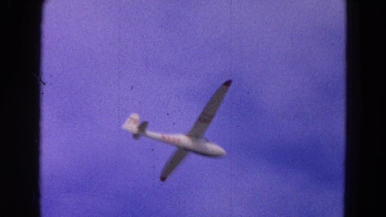 White glider tilting in open sky with faint clouds and film grain.