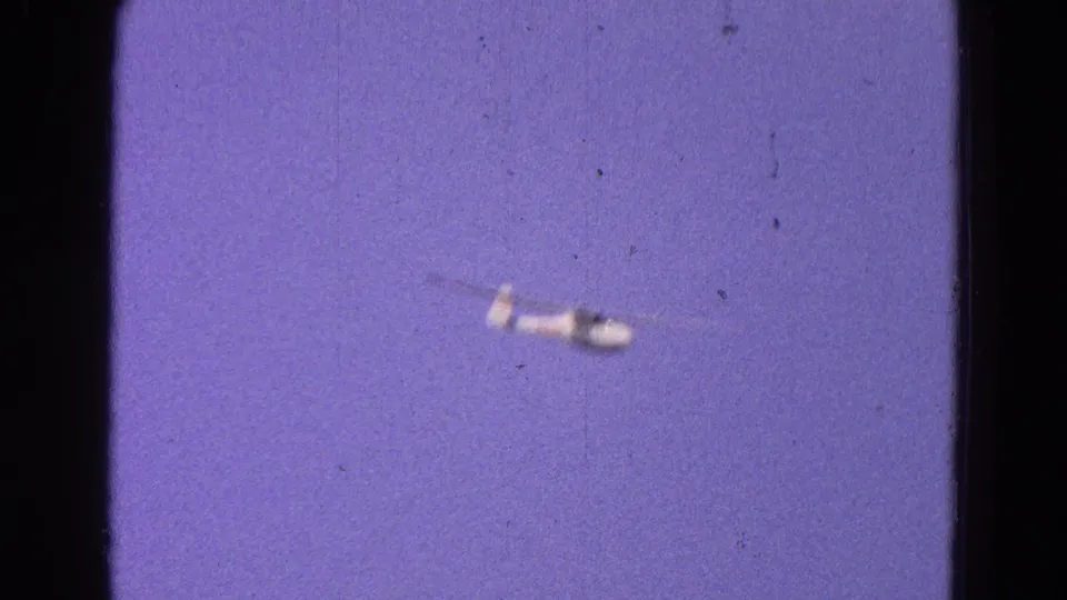 1964 Washington, DC 8mm frame of a distant white glider against a purple-blue sky, with soft focus and visible film specks.