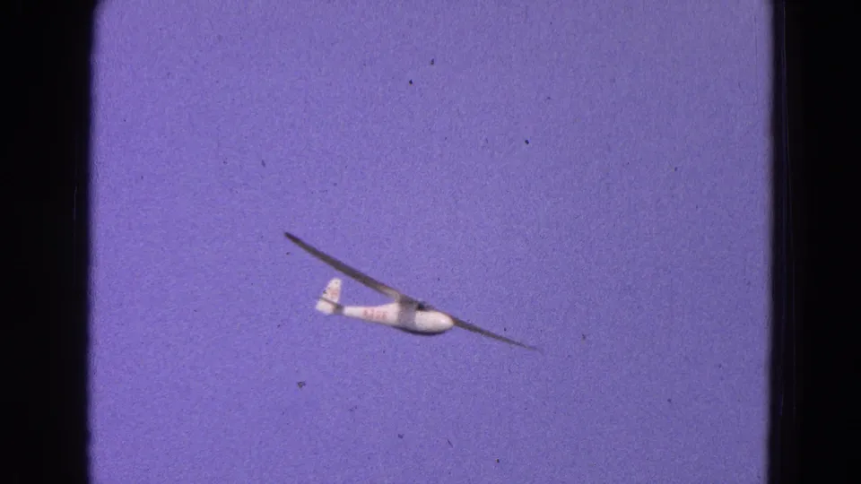 White sailplane banks across the Washington, DC sky in 1964 footage, with red aircraft markings and 8mm film texture.