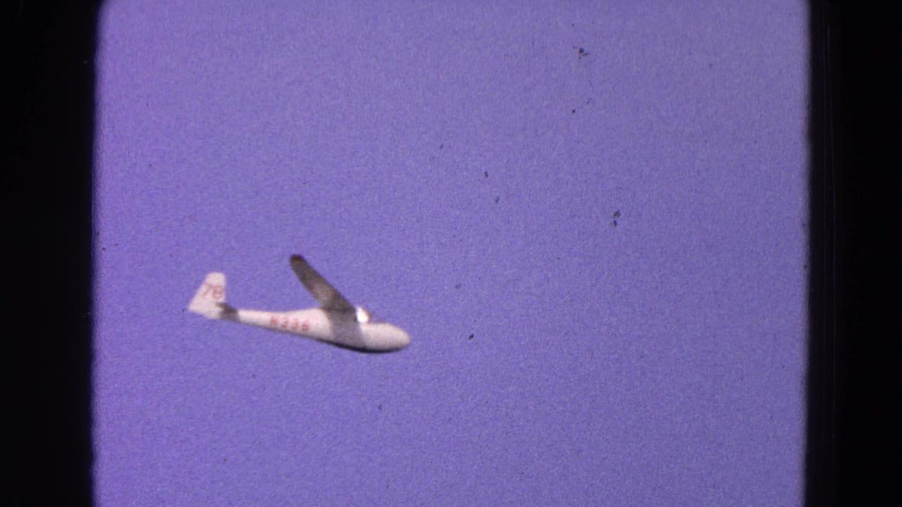 White glider with red markings flying across a purple-blue sky.