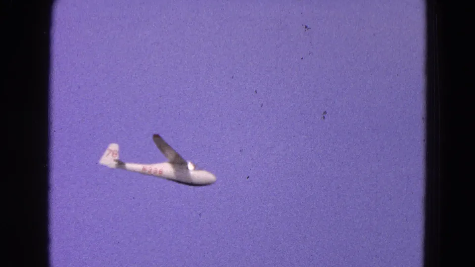 1964 8mm frame showing a white glider with red markings and tail number 78 against a purple-blue sky.
