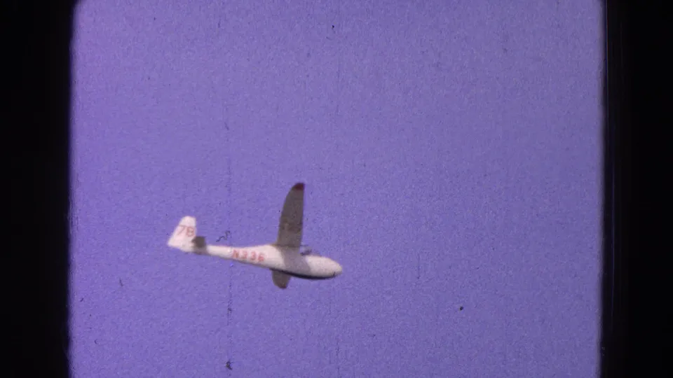 1964 8mm frame with a white glider in profile, red aircraft markings, and tail number 78 visible against open sky.