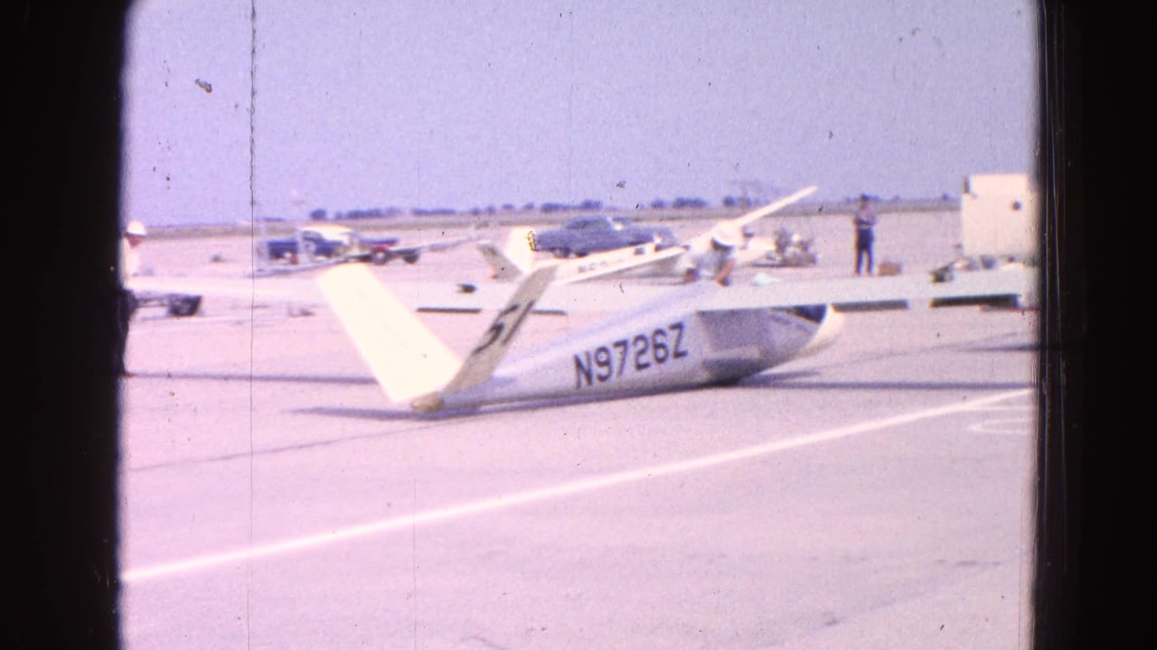 Glider on tarmac with its registration visible and small planes in the distance.