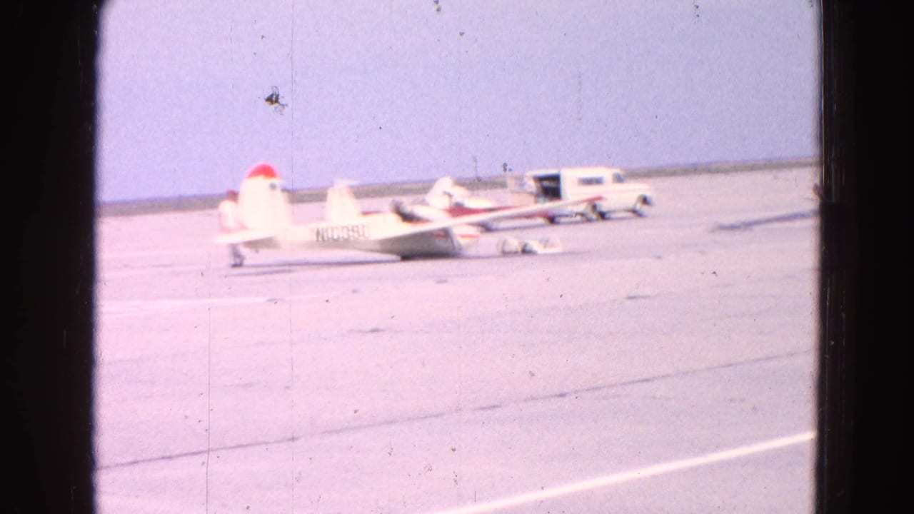 Rear view of a small white aircraft on the tarmac with another aircraft and van beyond it.
