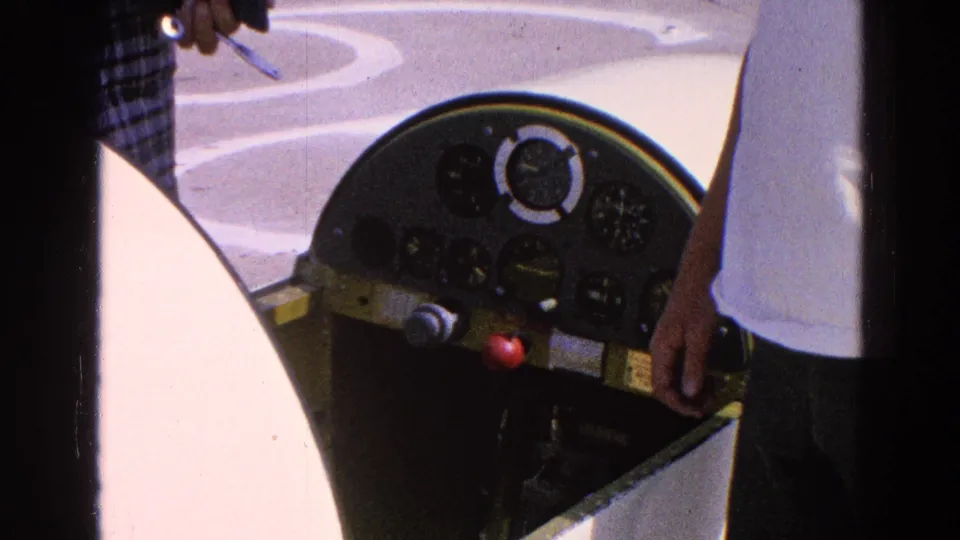 Close-up of the glider cockpit instrument panel with analog gauges, control area, and a person standing at the edge of frame.