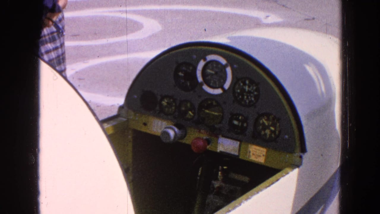 Side-angle cockpit detail from the 1964 Washington, DC clip, with analog gauges, pale aircraft bodywork, and a partially visible person nearby.