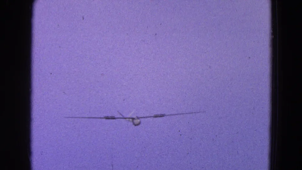 A small aircraft or glider appears distant in a purple-tinted sky, following the cockpit views in this 8mm aviation clip.