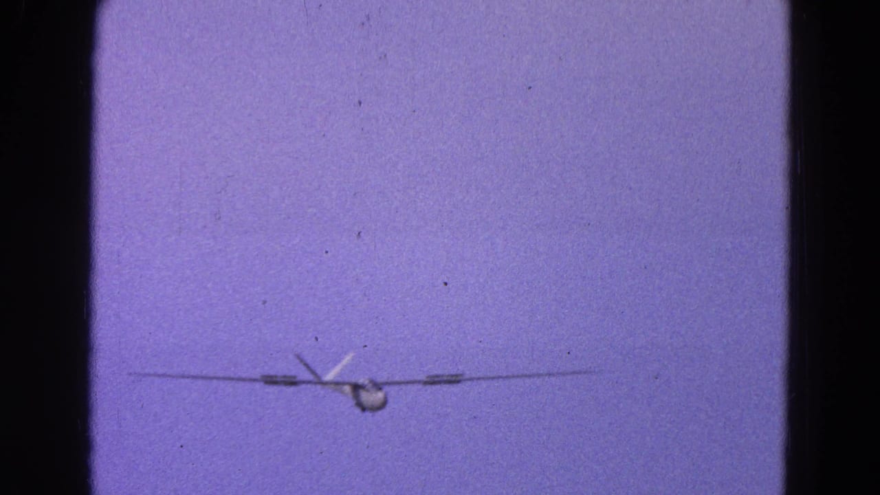 Distant light aircraft in a 1964 Washington, DC 8mm frame, with purple color cast and visible film gate edges.