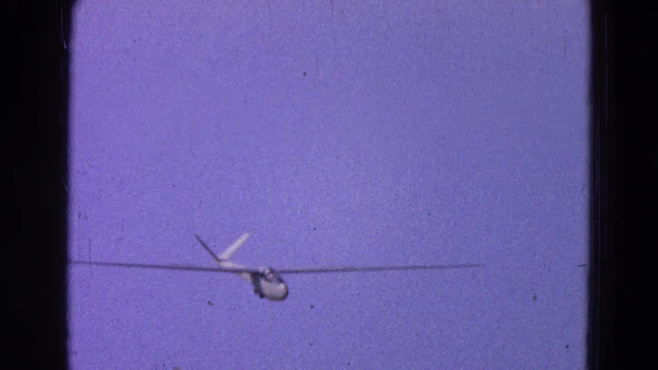 Distant small plane near the lower center of a Washington, DC 1964 8mm frame, with grain and faded color visible.