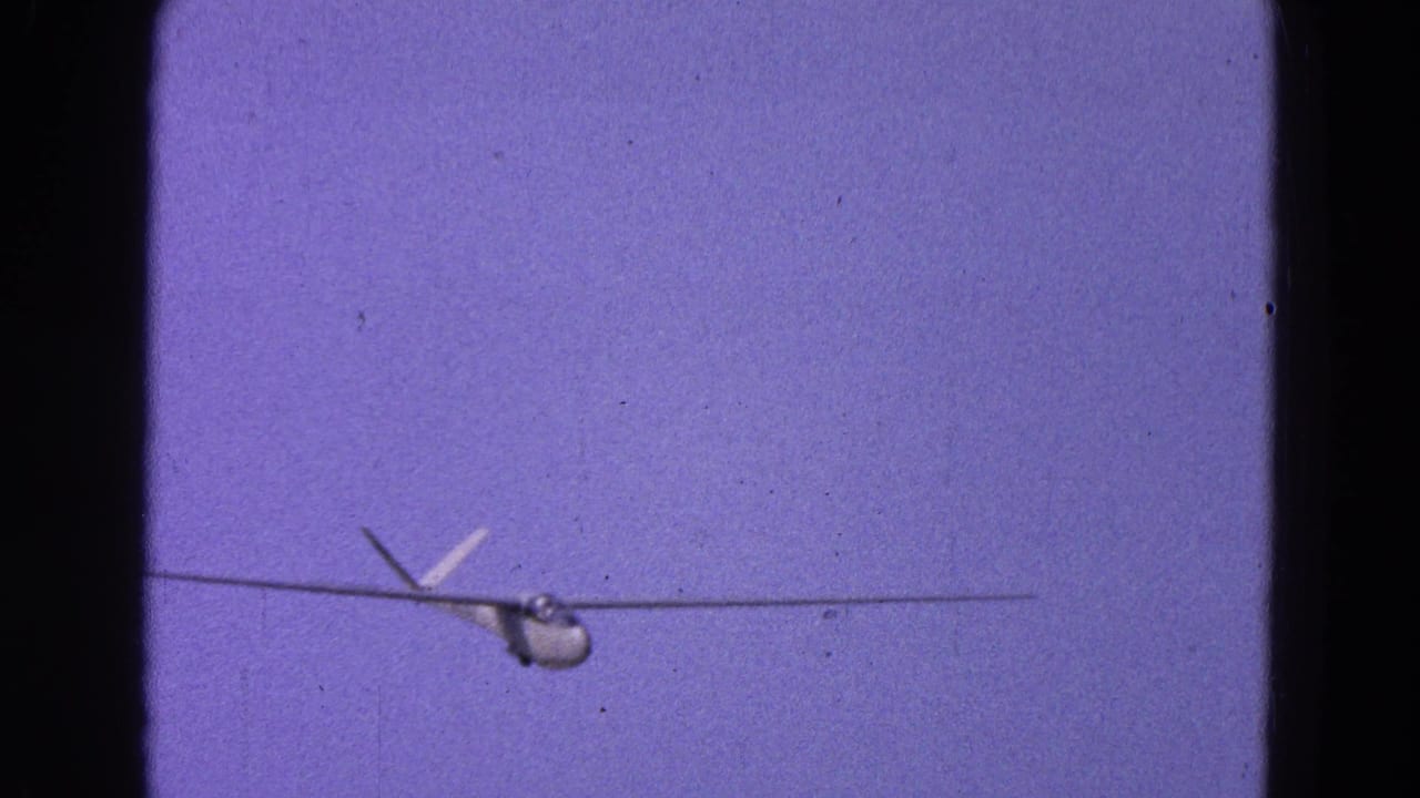 Small glider seen head-on against a purple-blue sky within an 8mm film frame.