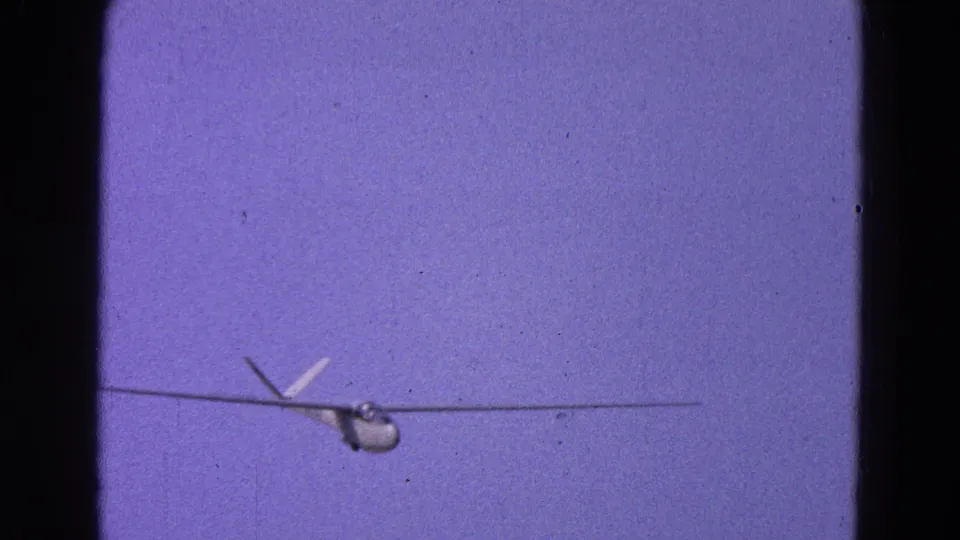 1964 Washington, DC-area 8mm frame showing a glider approaching from a distance against a purple-blue sky.