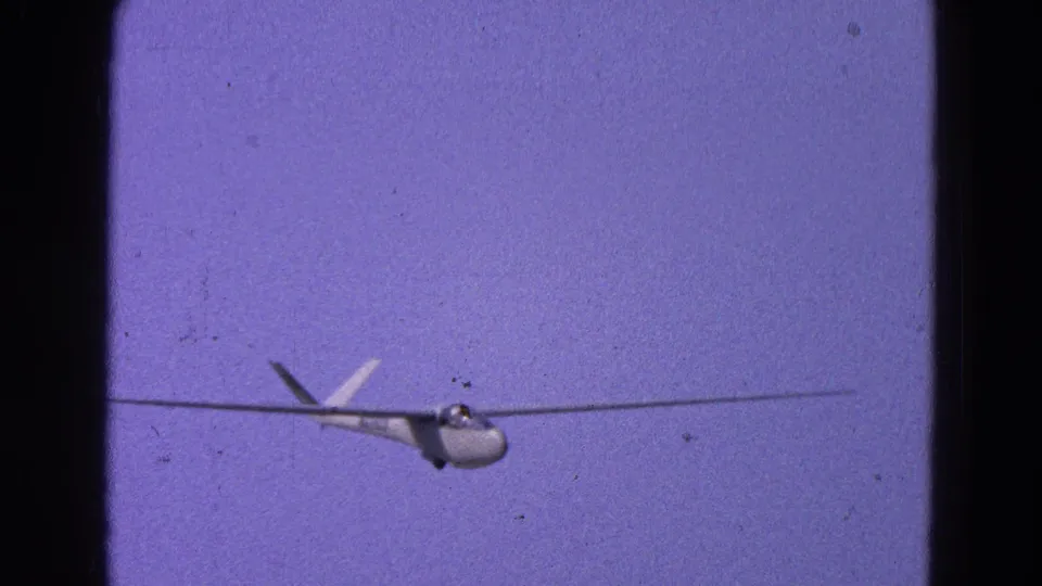 The glider appears larger in frame as it descends, with 8mm grain and dark film borders visible.