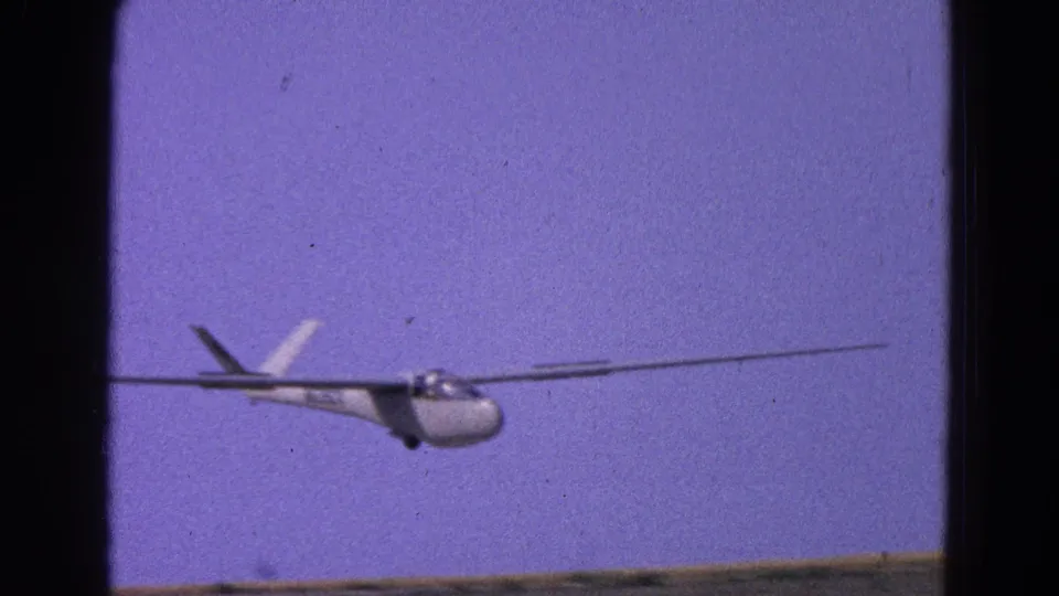 A 1964 8mm view of the glider nearing the runway, with a thin ground line visible below the aircraft.
