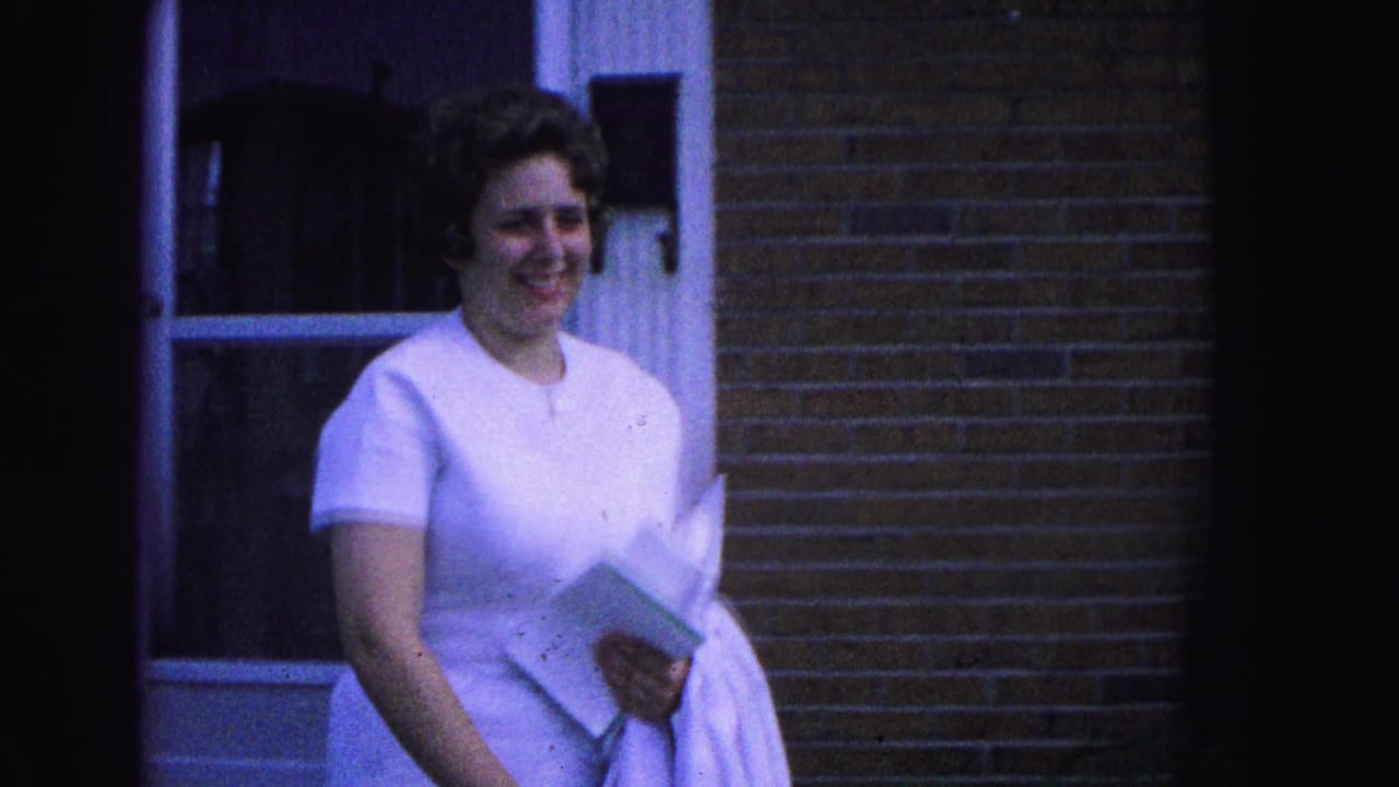 Woman in a white dress smiles outside a brick house doorway.