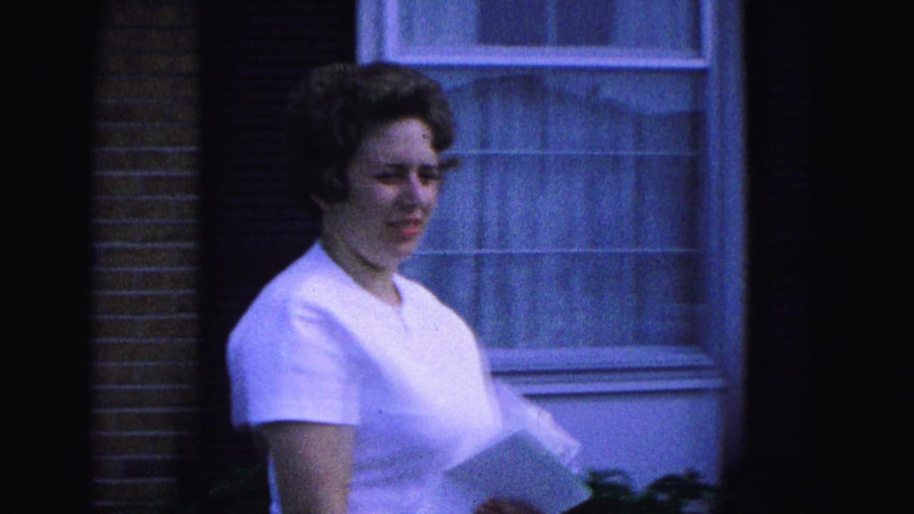 Woman in a white dress walks past a window holding papers.
