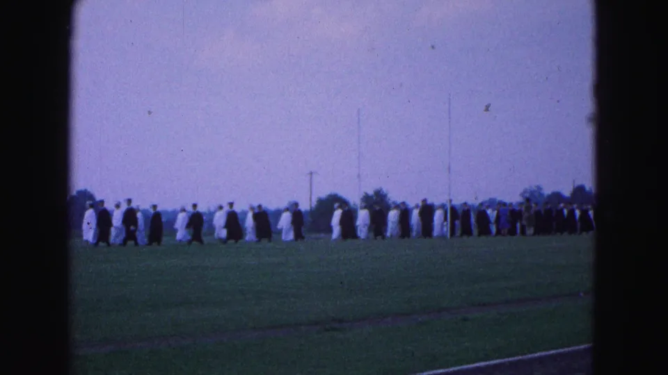 A wider 8mm view shows robed graduates crossing the outdoor ceremony field in Williamsburg, Virginia.