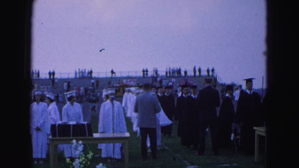 Closer graduation footage shows robed students and adults near ceremony tables, with flowers and bleachers in the background.