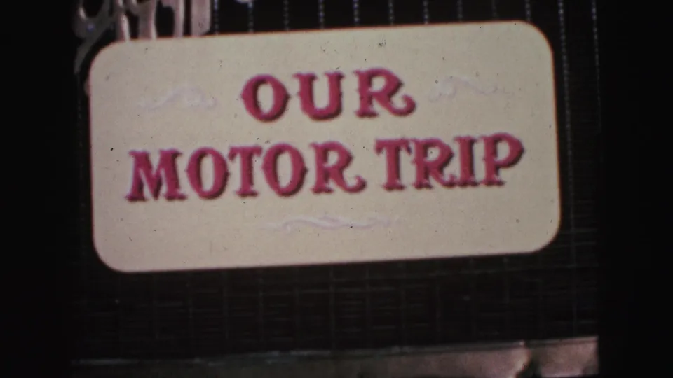 Close view of the 1964 motor-trip title card, showing raised pink text and light scroll details within the 8mm frame.