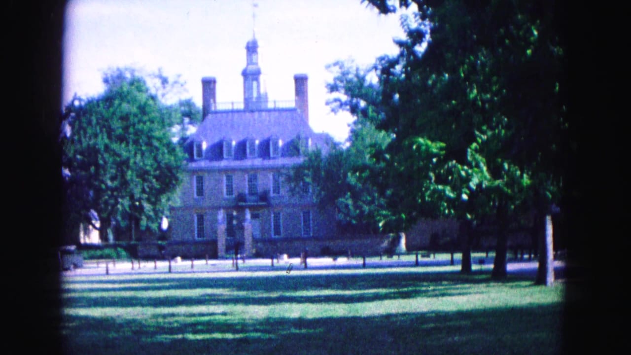 Wide view of a brick historic building across a lawn with trees and film-frame borders.