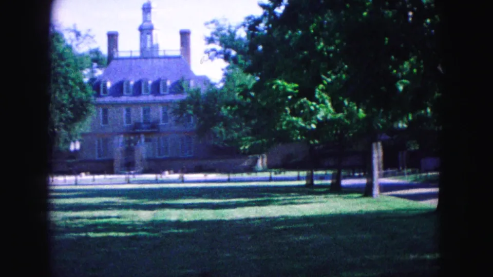 1964 Williamsburg frame of a colonial-style brick building with cupola, partly obscured by trees and dark film borders.