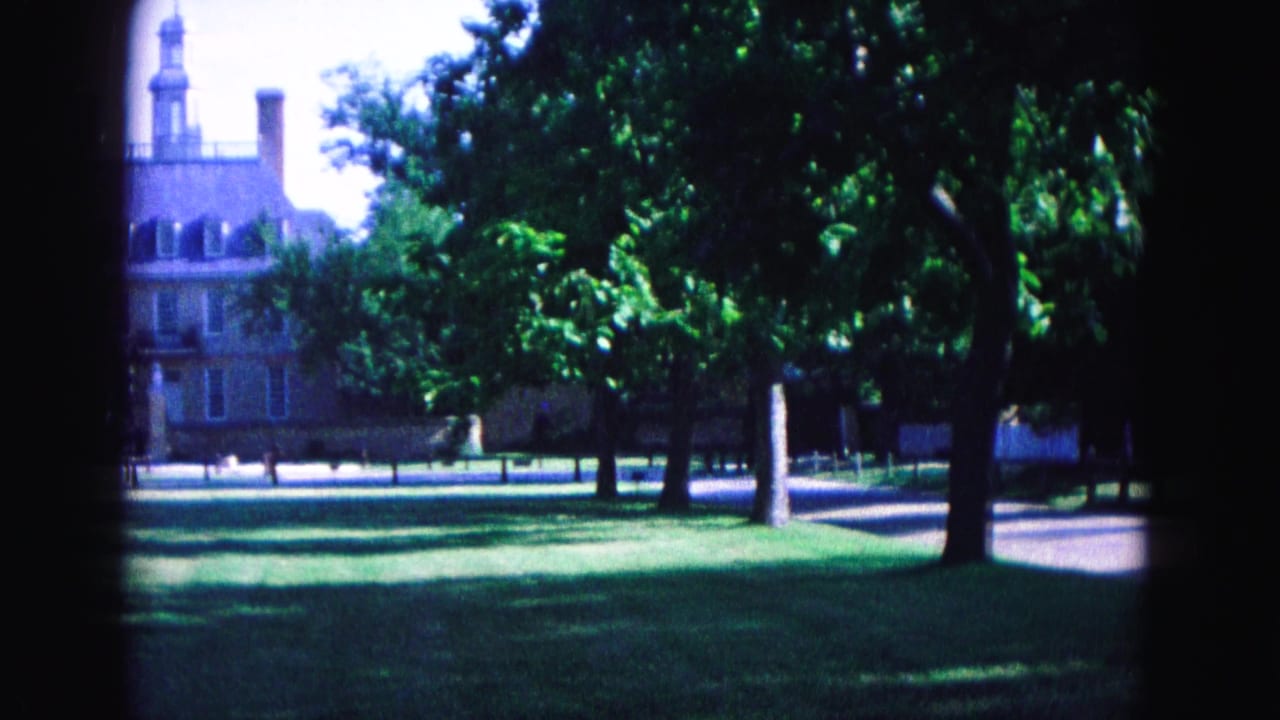 Historic building with cupola partly visible beyond trees and lawn.