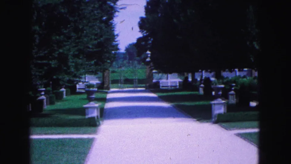 The final frame shows the Williamsburg garden walkway receding under trees, with clipped hedges, lawn, stone posts, and a white fence behind.