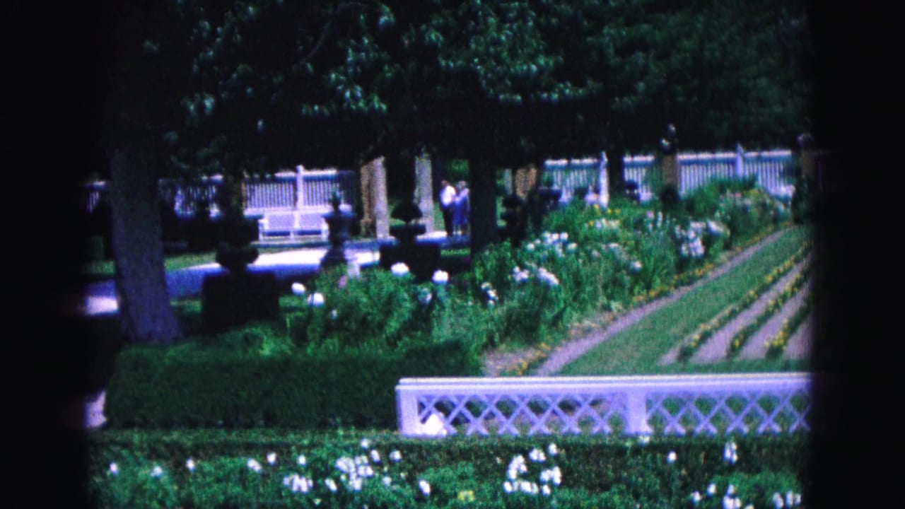 Garden beds and white fencing with visitors partly visible among trees.