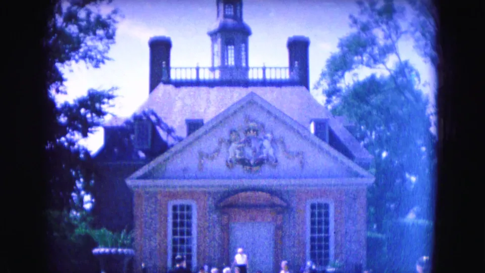 1964 Williamsburg view of a brick church-like building with ornate pediment, cupola, chimneys, flanking windows, trees, and bright sky.