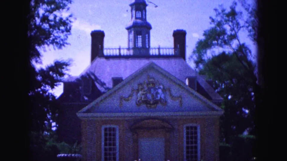 Williamsburg 1964 frame of a brick church-like facade with cupola, paired chimneys, decorative pediment, trees, and darker 8mm exposure.