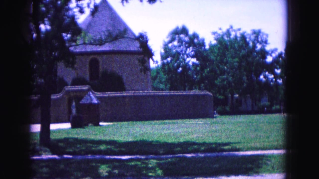 The camera has panned slightly right across a Williamsburg historic grounds view, keeping the walled building and lawn in frame.