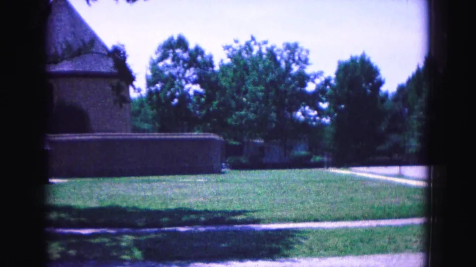 A later frame from the 1964 Williamsburg clip shows the building partly cropped as the pan opens onto lawn, trees, and roadway.