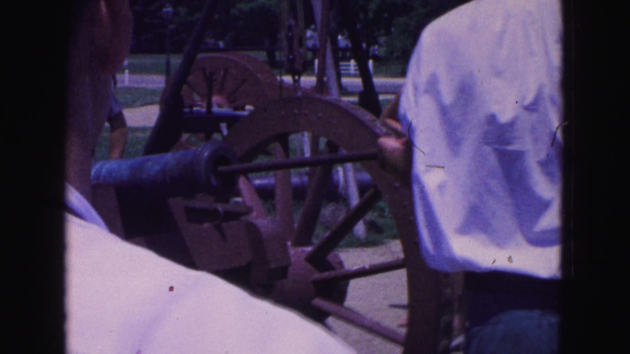 Visitors stand near an old cannon as a man in a white shirt faces the cannon.