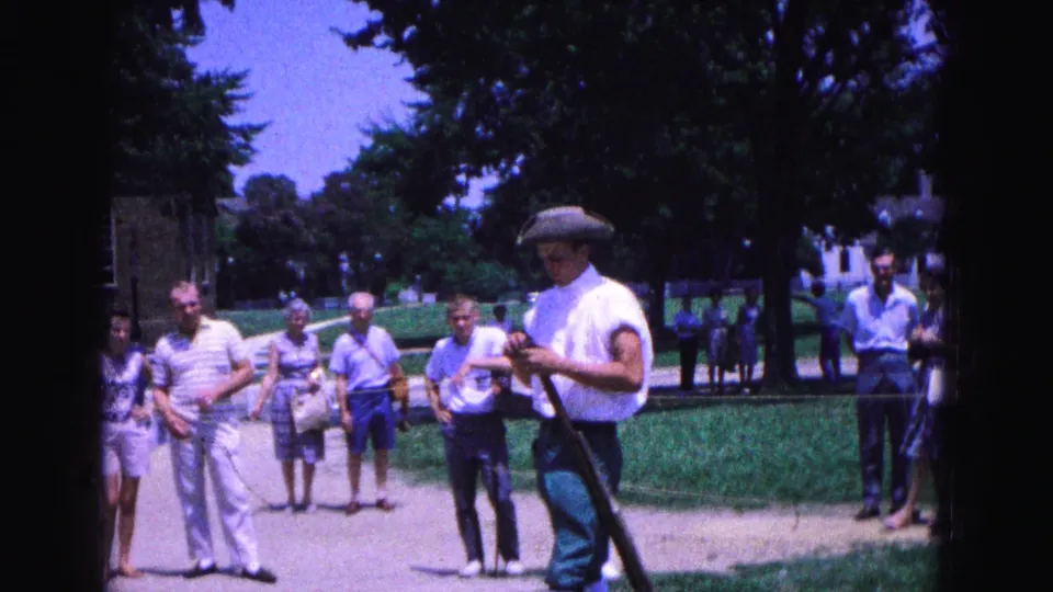At the end of the Williamsburg clip, the costumed man turns with the long gun as casually dressed tourists remain on the path.