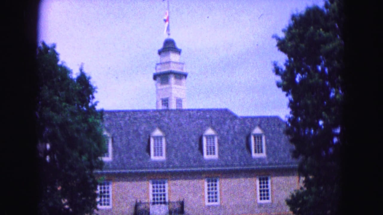 1964 Williamsburg, Virginia home-movie frame showing a brick historic-style building with dormers, cupola, and trees at the edge of the view.