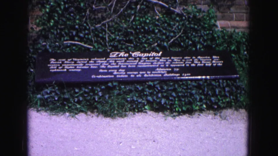 Close 1964 8mm view of the Capitol sign, with white text on a dark panel set before ivy and brick.