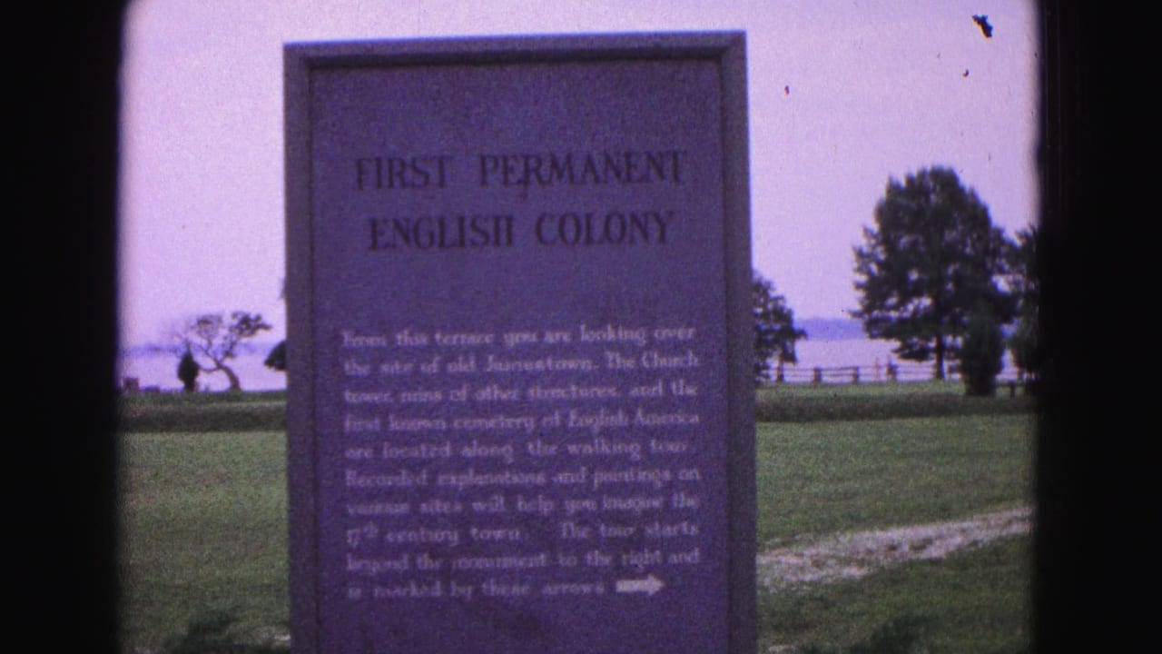 1964 Williamsburg frame showing the First Permanent English Colony marker on a lawn with trees, fencing, and distant water in the background.