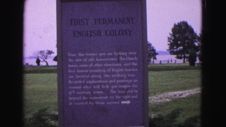 1964 Williamsburg 8mm frame with the First Permanent English Colony marker in close view and waterfront grounds behind it.