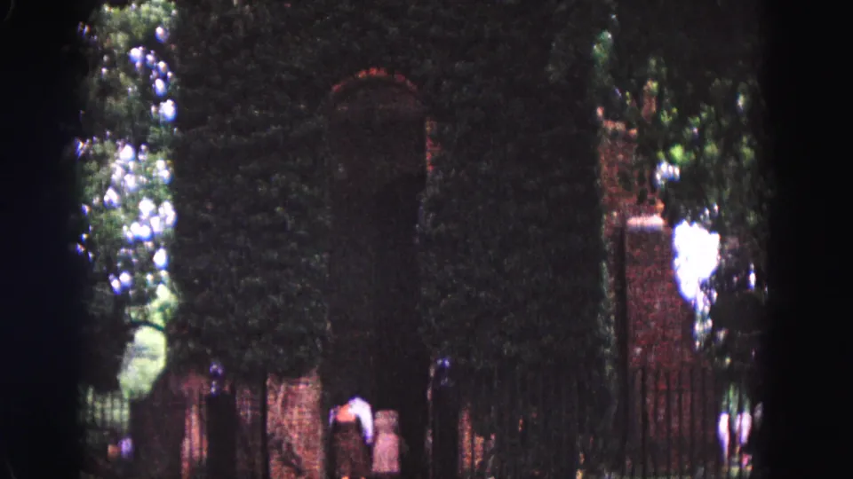 The closing frame shows visitors near a shaded, ivy-covered brick wall and arched gate in the supplied 1964 Williamsburg home-movie footage.