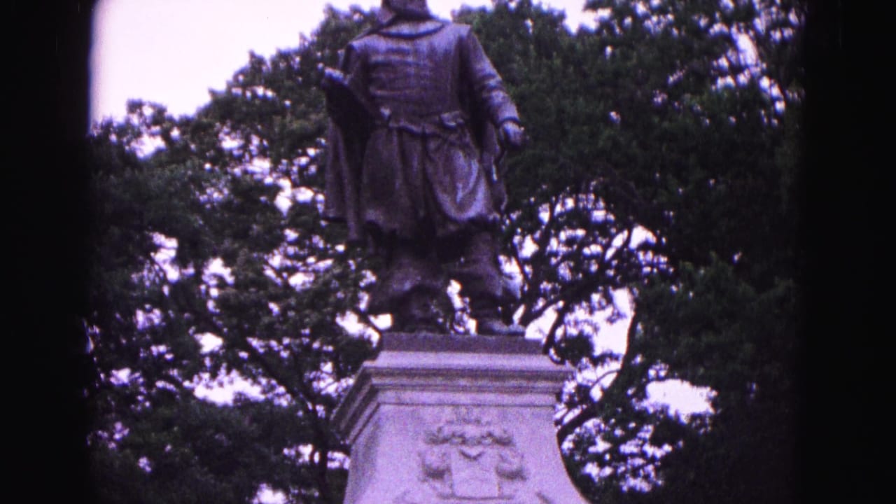 Bronze statue on a stone pedestal among trees.