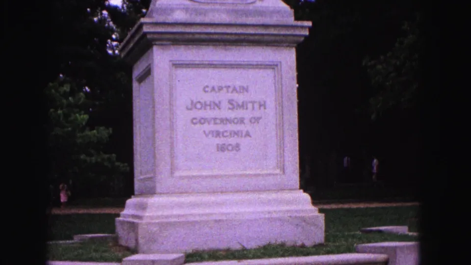 The Williamsburg monument pedestal remains centered, with its inscription legible and small distant visitors visible near the trees.