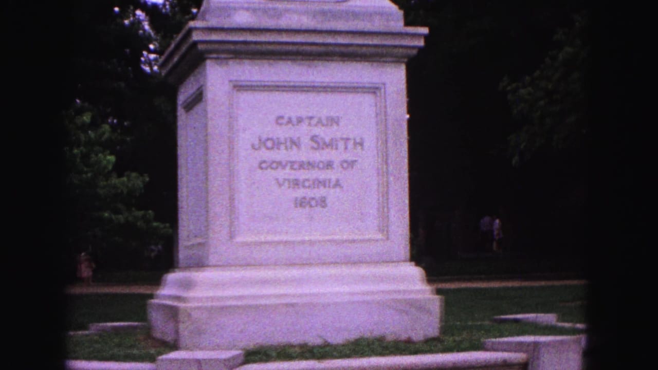 Stone pedestal for Captain John Smith monument in a grassy park with trees behind it.