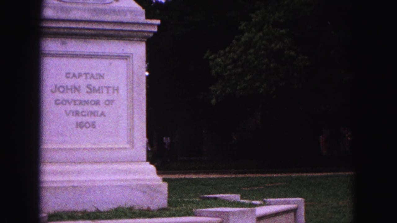 The Williamsburg monument pedestal remains centered, with its John Smith inscription readable and park trees dark behind it.