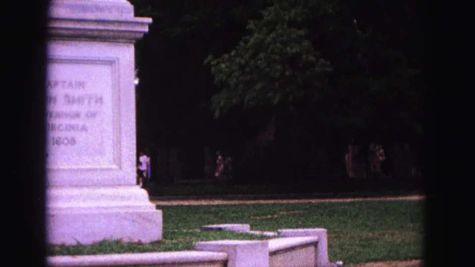 Handheld 8mm frame shifts left, cropping the monument while showing the surrounding lawn, trees, and visitors in the background.