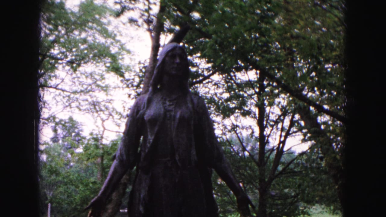 Bronze woman statue framed from the upper body among trees and lawn.