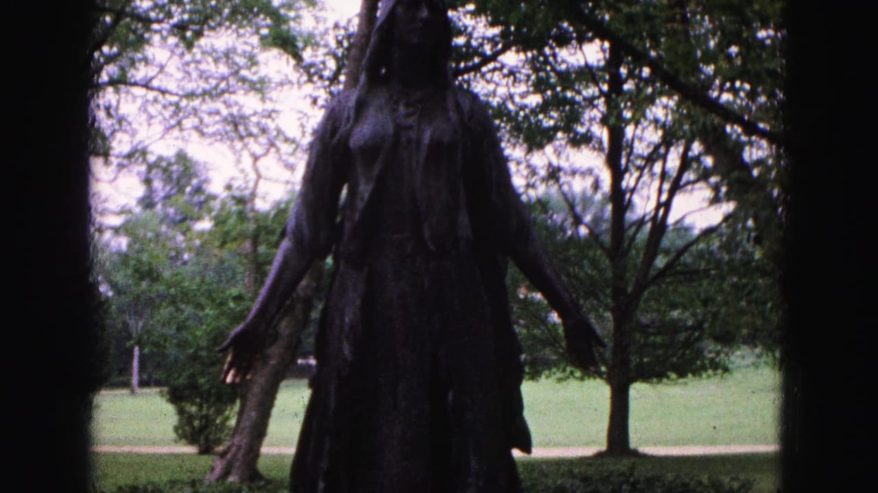 Bronze statue seen from the torso down with trees, grass, and a path behind it.