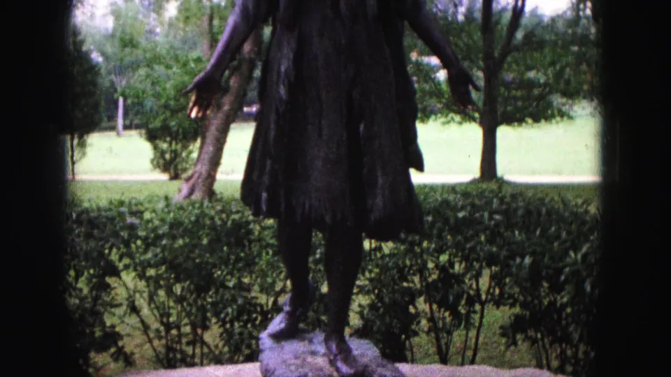 1964 Williamsburg frame showing the bronze female statue from head to feet on a pedestal in a landscaped park.