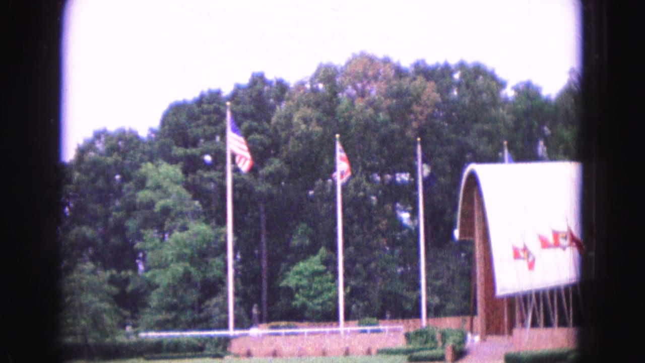 Flagpoles and curved-roof building beside trees and lawn.