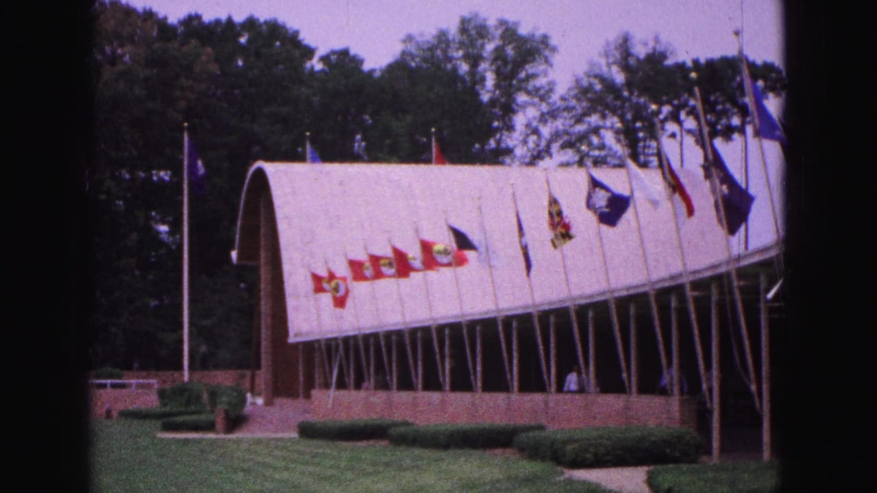 Rows of flags line the front of an arched building beside a lawn.